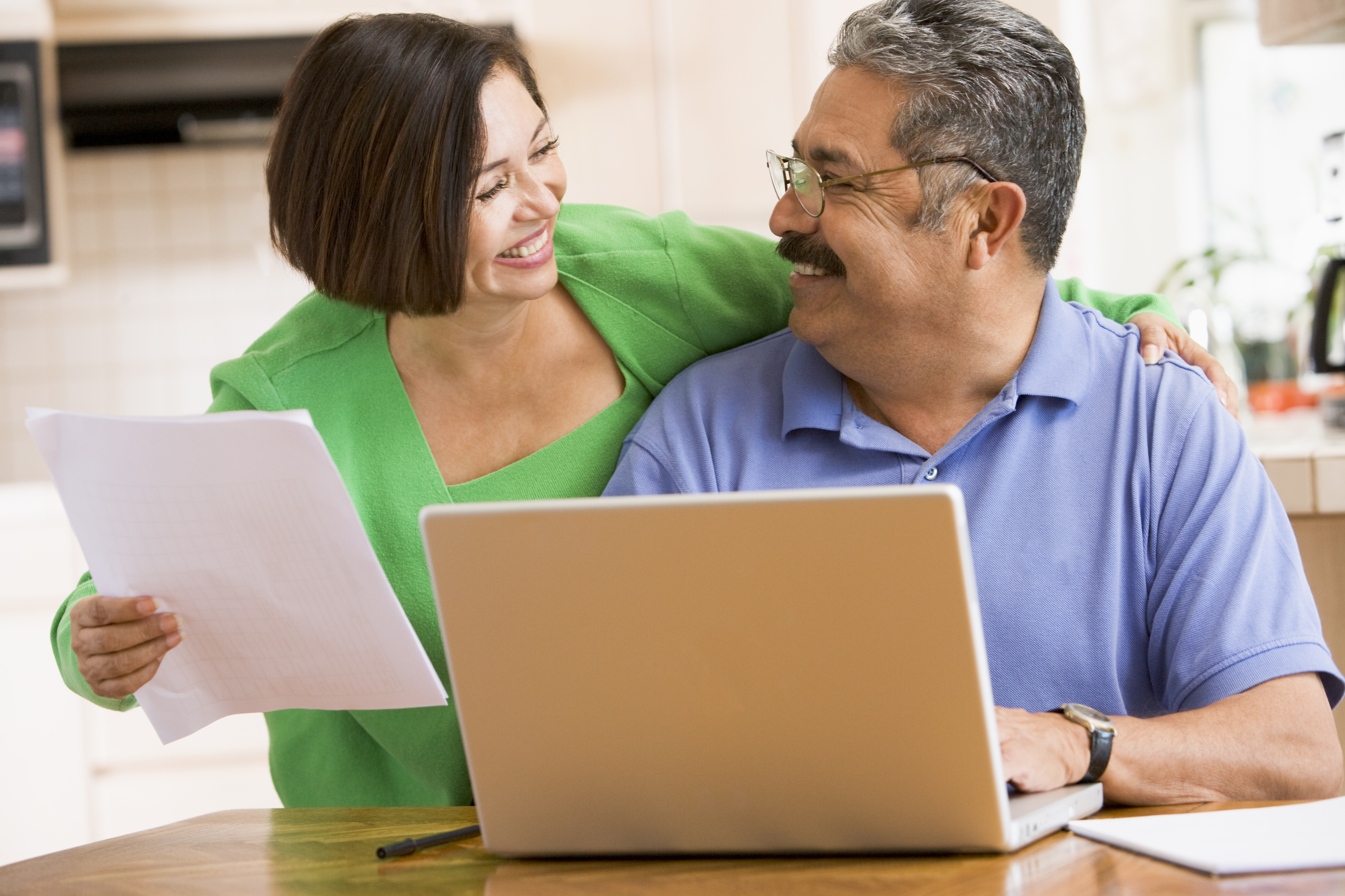 couple in kitchen with laptop and paperwork smiling BKG93c0rj